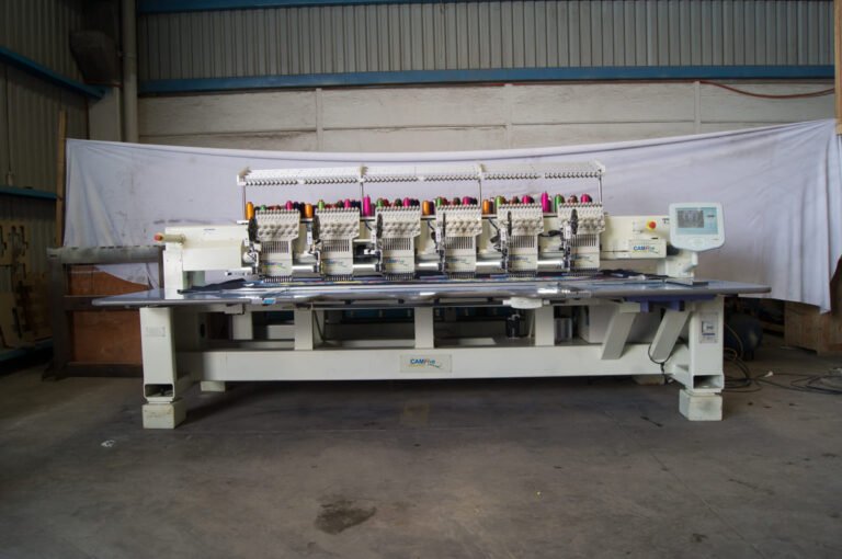 Bordadora plana CAMFive bordando sobre lienzos con accesorio de lentejuela y panel táctil visible.
