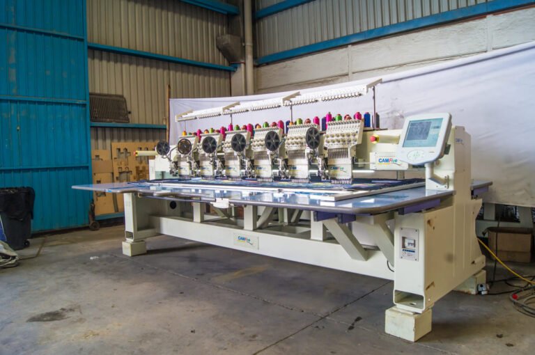 Bordadora plana CAMFive bordando sobre lienzos con accesorio de lentejuela y panel táctil visible.