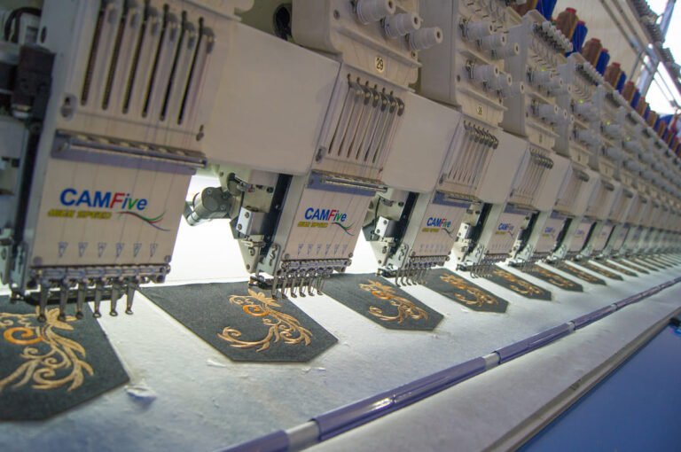 Varios cabezales de una bordadora plana CAMFive trabajando al mismo tiempo, bordando el mismo diseño en tela.