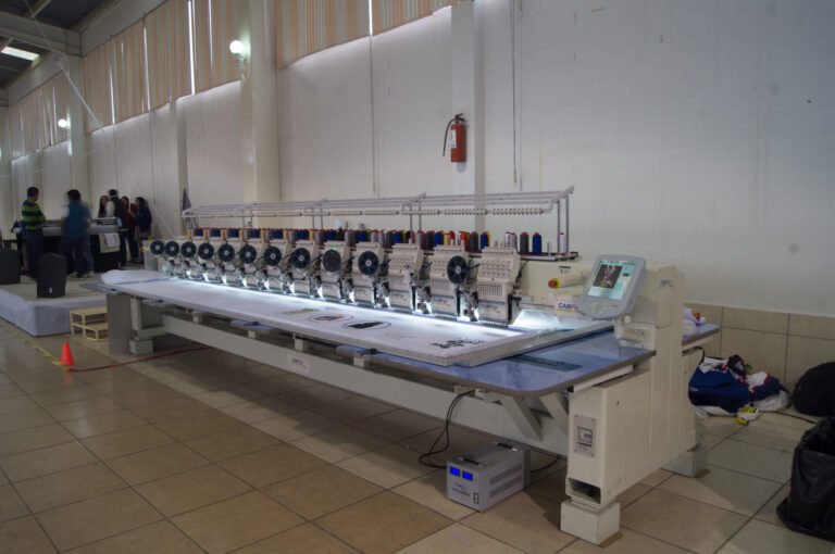 Bordadora plana CAMFive bordando sobre lienzos con accesorio de lentejuela y panel táctil visible.